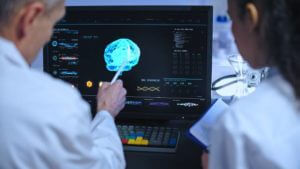 Senior scientist drawing intern's attention to 3D brain image, working in neurology diagnostics lab