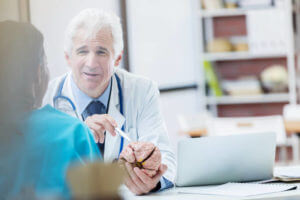 Confident Caucasian senior male neurosurgeon consults with a colleague about a patient's diagnosis. The male doctor is holding a human brain model.