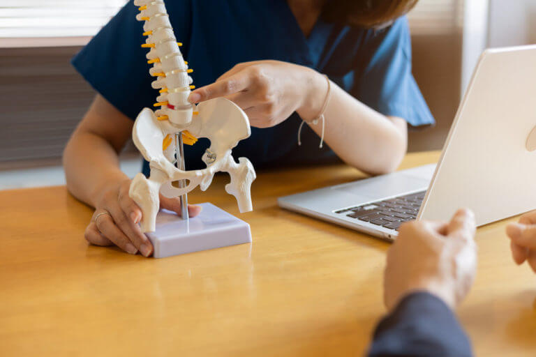 Close-up physical therapist's hand pointing to the back of a human skeleton to advise and consult the patient about back pain treatment.