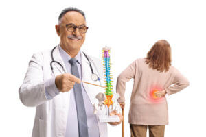 A senior male back surgeon is holding and explaining a spine model to a senior female patient prior to back surgery.