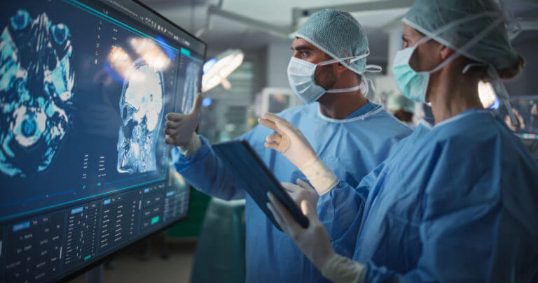 Image of a female and male Surgeons Reviewing Brain Scans for Tumors in a Dimly Lit Operating Room.