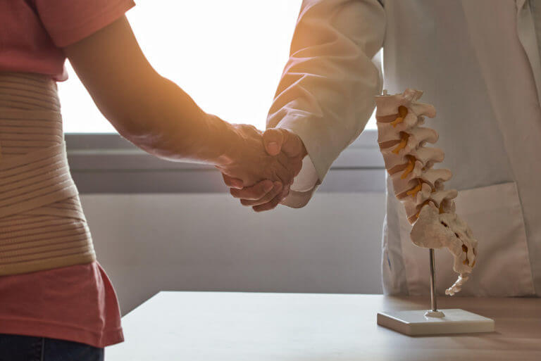 A leading spine surgeon greets a patient suffering from back pain in a medical office.