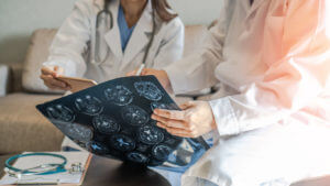 A professional brain and neurological surgeon with a digital tablet is working in a hospital clinic, discussing and diagnosing a patient's brain tumor surgery care.