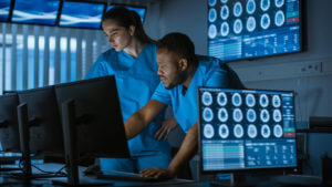 Two neurosurgeons are discussing neurological conditions while working on a personal computer in a modern laboratory.