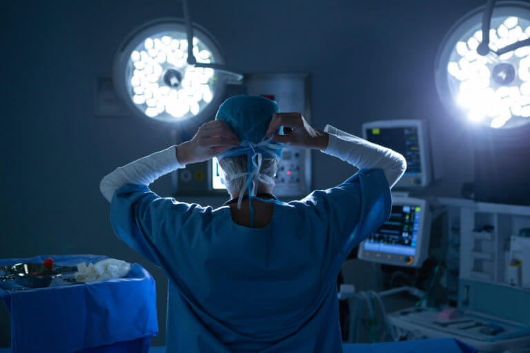 A female neurosurgeon wearing a surgical mask in the operating room is preparing for spine surgery.