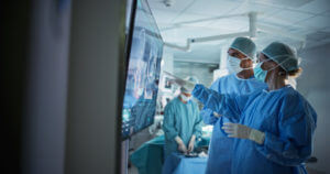 Two Neurosurgeons Looking at a Patient's Scans on a Large Screen in a Dimly Lit Operating Room For Surgery for Aneurysm in the Brain.