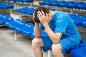 A man with head pain from concussion after workout on a sports ground.