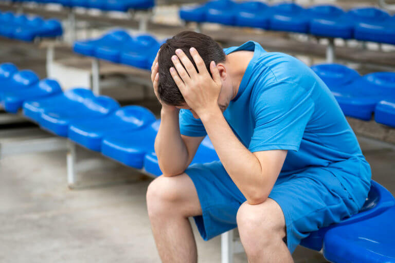 A man with head pain from concussion after workout on a sports ground.