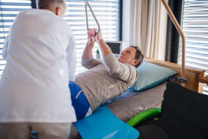 A healthcare worker helping a senior patient with spinal cord injury during rehabilitation program in hospital.